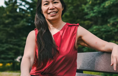 A woman in a red shirt sitting on a bench outside.