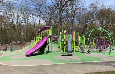 A purple and green playground equipment. Trees line background of photo.