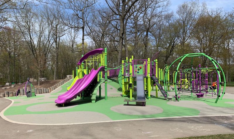 A purple and green playground equipment. Trees line background of photo.