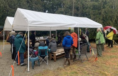 two white tents under which several people sit and stand