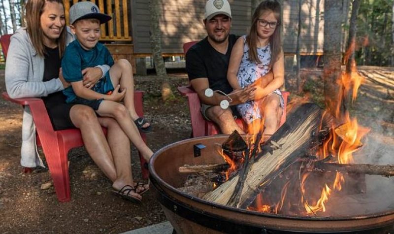 Une famille assise devant un feu à côté d'un chalet en forêt