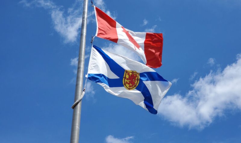 Nova Scotia and Canada flags flying on a flag pole against a blue sky