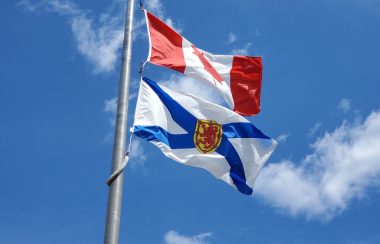 Nova Scotia and Canada flags flying on a flag pole against a blue sky