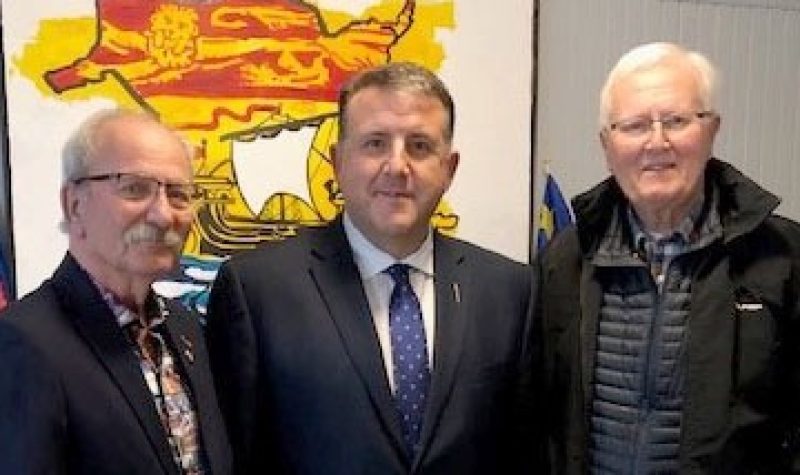 Three men pose for a photo in front of NB logo.