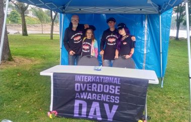 Photo of four people wearing NANDU shirts behind a table with a banner reading International Overdose Awareness Day.