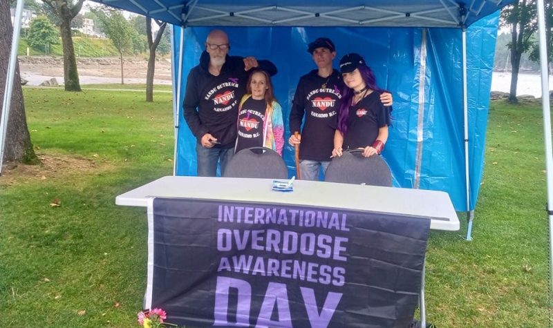 Photo of four people wearing NANDU shirts behind a table with a banner reading International Overdose Awareness Day.