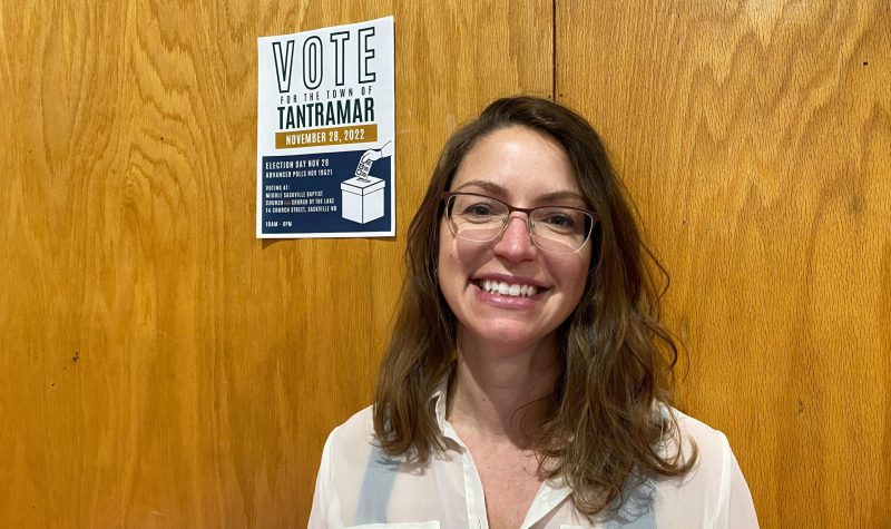 A woman, smiling, standing in front of a wall with a poster reading VOTE.