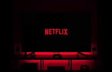Un écran de télévision affichant le logo de Netflix en rouge sur un écran noir dans une pièce sombre lègèrement éclairé en rouge