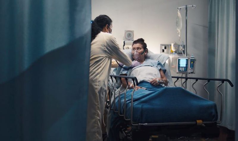 a patient on a hospital bed looks to her nurse for help, but who will help the nurses?