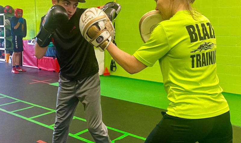Noah DiNola in an active fighting stance. DiNola stands with a trainer in an action shot taken in a striking lime green-painted gymnasium.