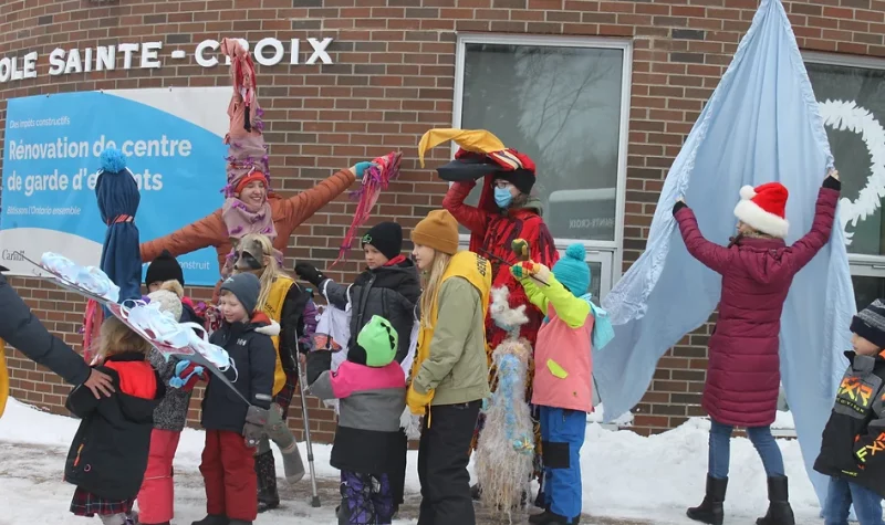 On peut voir des élèves de l'école Sainte-Croix de Lafontaine, à l'extérieur, en compagnie d'animateur de l'activité « Noël au village » . La photo à été prise en face de l'école Saint-Croix et tous semble avoir du plaisir.