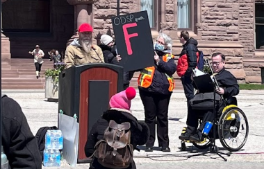 People at a podium speaking and holding up a sign with the letter F.