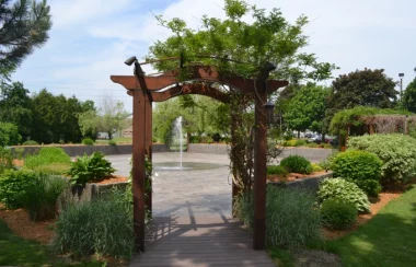 An archway leads into a courtyard with a fountain in the center, various mostly green plants surround the peremiter of the courtye=ard in a circular shape. It is a sunny day with blue skies.