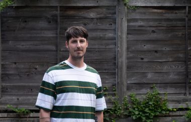 A man with a stripped shirt in front of a wooded background.