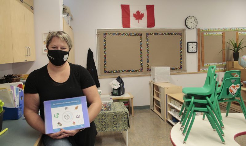 Une enseignante, masque au visage, présente du matériel scolaire relatif aux règles de Santé publique.