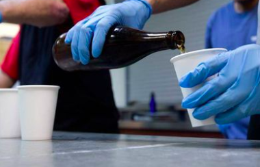 Blue gloved hands pour beer into plastic cups
