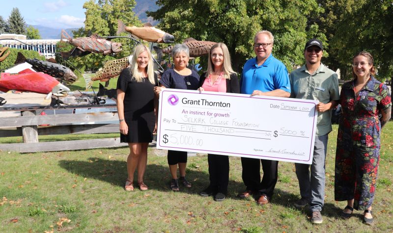 A group of people holding a large cheque. Indigenous art and trees in the background.