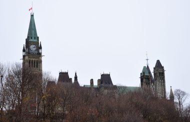 The parliament buildings in Ottawa can be seen behind a treed hill on a gloomy day.
