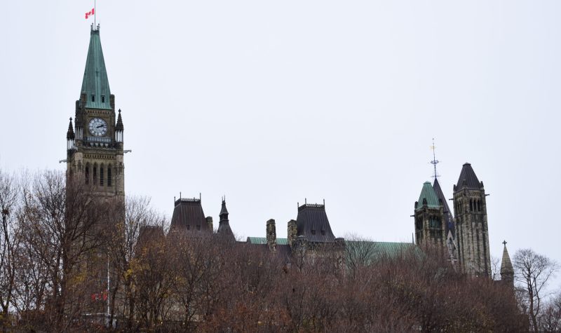 The parliament buildings in Ottawa can be seen behind a treed hill on a gloomy day.
