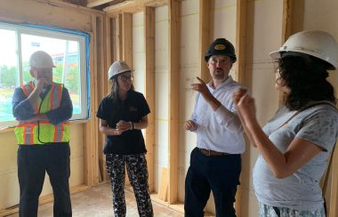 4 people stand together wearing construction helmets inside a room under construction