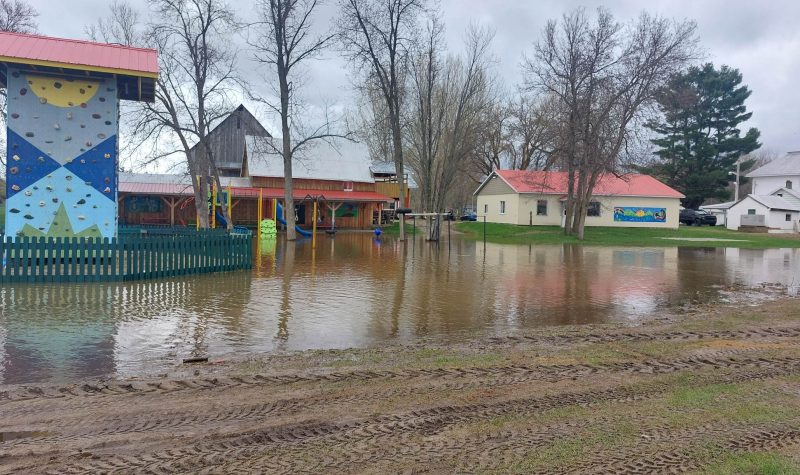 An outdoor climbing wall stands in the foreground with buildings in the background and flood water filling up the ground around them.