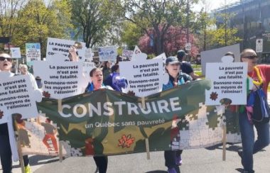 Les manifestants défilent dans la rue. Les pancartes mises de l'avant ont comme message « La pauvreté n'est pas une fatalité. Donnons-nous les moyens de l'éliminer ». Au milieu, la banderole de l'organisme où on peut y lire « Construire un Québec sans pauvreté ».