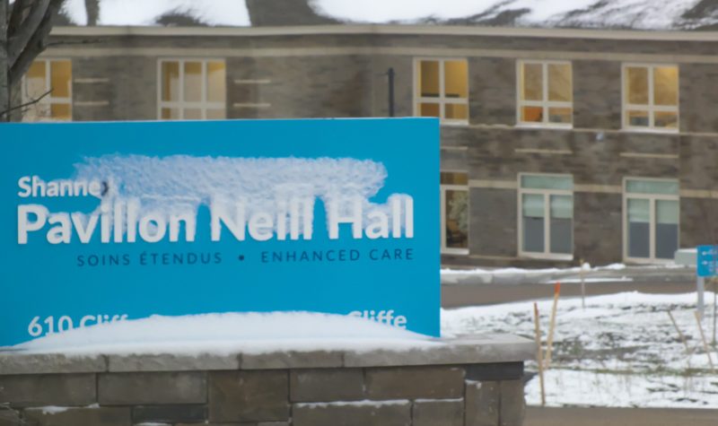 Un panneau enneigé sur lequel il est écrit : Pavillon Neill Hall, en arrière-plan le pavillon