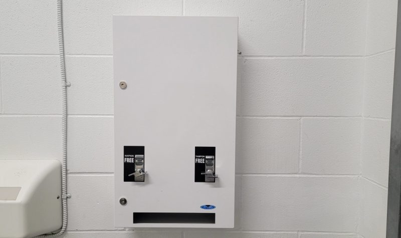 White metal dispenser with one tampon knob and one pad knob mounted on a white wall