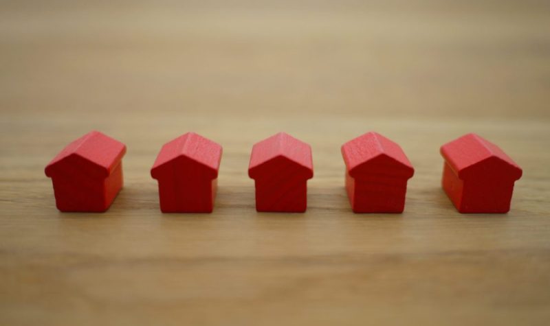 On voit cinq petite maison de bois rouges alignées sur une table en bois