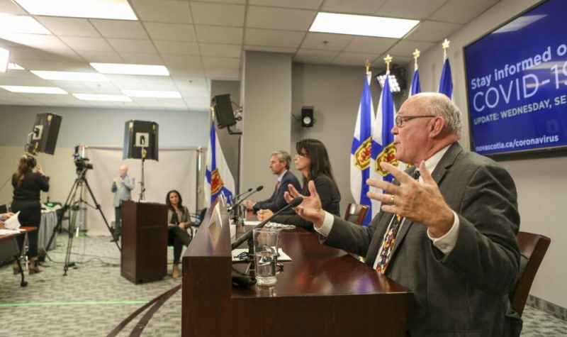 Deux hommes et une femme , assis devant des micros, répondent aux questions des journalistes dans une salle avec drapeaux de la Nouvelle-Écosse.