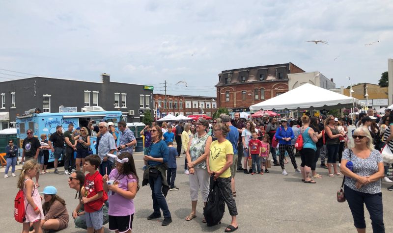 On voit des dizaines de personnes de tous âges dans un stationnement de la rue King à Midland qui sont debouts et attendent le prochain spectacle de musique