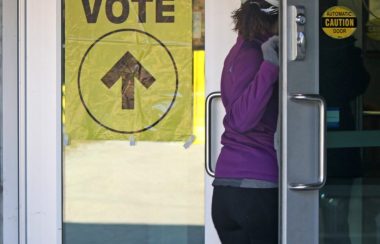 Une électrice suit la consigne d'une affiche jaune d'Élections Canada lui indiquant l'endroit du vote.