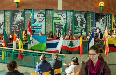 De jeunes étudiants internationaux lèvent des drapeaux représentant le multiculturalisme du Campus Saint-Jean