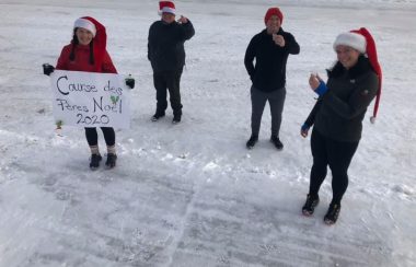 Quatre membres du comité du Club de course de Forestville portant un bonnet de père-noël à l'extérieur et tenant un petit verre. Une affiche indique Course des Père-Noël 2020