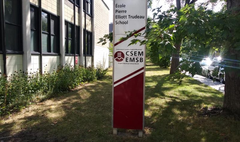 L'enseigne de l'École Pierre-Elliott-Trudeau entre l'édifice et un arbre.