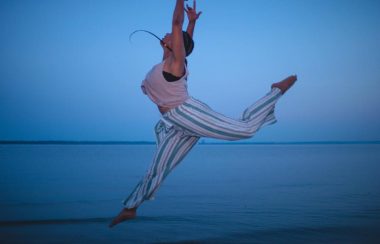 Chloé Saintesprit, danseuse, en mouvements avec les bras vers le haut, au bord de mer
