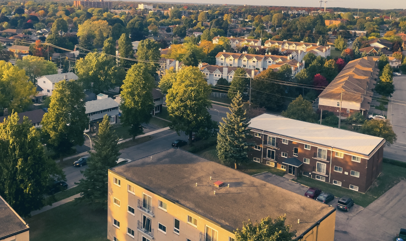 An aerial view of a treed city with four story apartment buildings in the foreground.