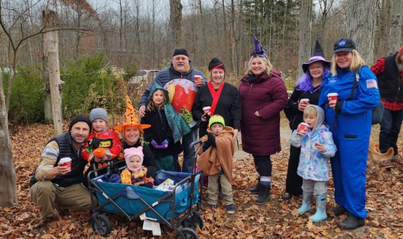 On peut voir quelques familles ayant participé à la marche « Step up for Down Syndrome » au Tiffin Centre. La photo a été prise dans un boisé. On peut voir les feuilles mortes au sol et certains parents portent un costume d'Halloween.