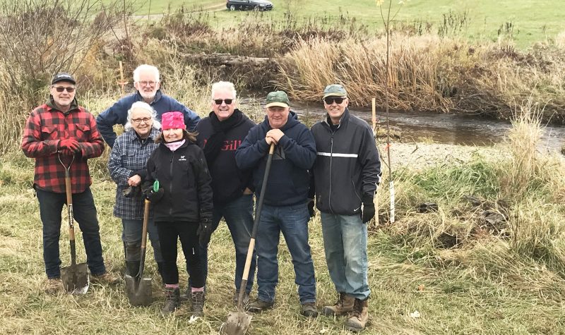 Seven of the volunteers that took part in tree planting along Quilliams stream. With shovels in hand, they stand in front of the stream.