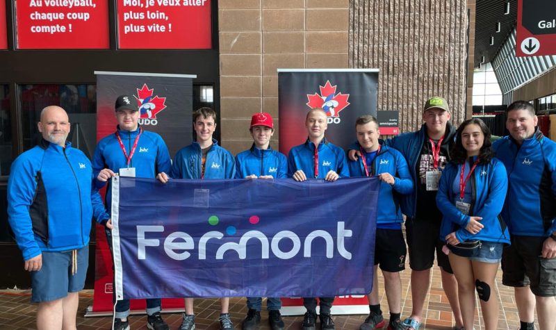 Groupe de jeunes athlètes et leurs entraîneurs avec un grand drapeau avec le logo de Fermont