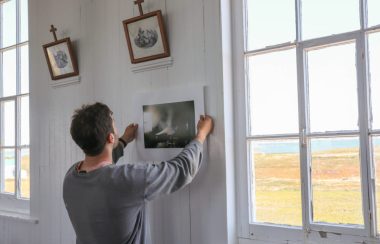 Un photographe vu de dos recadre une photo de son exposition, à côté d'une fenêtre