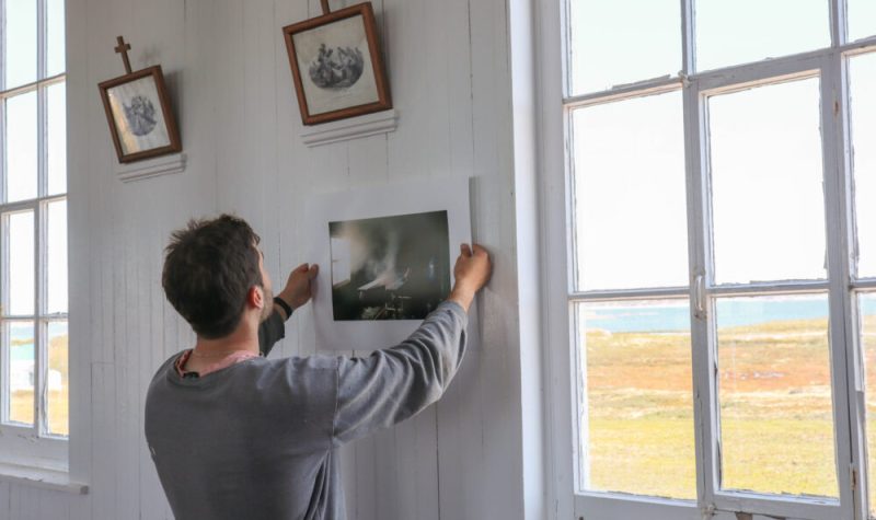 Un photographe vu de dos recadre une photo de son exposition, à côté d'une fenêtre