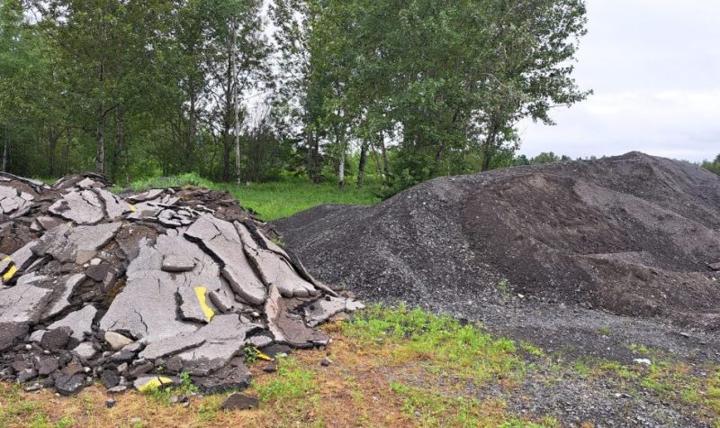 Un tas d'asphalte déchiqueté à gauche ainsi qu'un tas d'asphalte recyclé à droite, à l'extérieur lors d'une journée d'été nuageuse