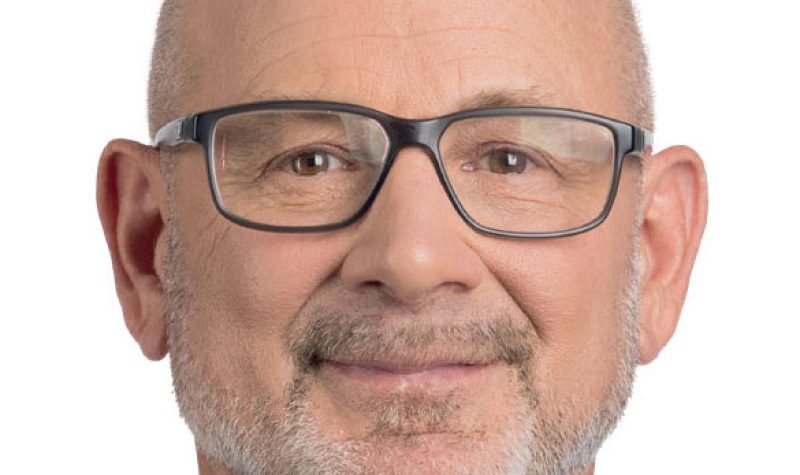 Pictured is a headshot of Quebec Liberal Party candidate. He is wearing black square glasses and a suit against a white background.