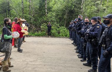 rang de policiers face à un rang de manifestants et la forêt en arrière-plan