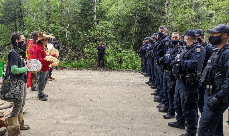 rang de policiers face à un rang de manifestants et la forêt en arrière-plan