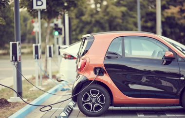 Une petite voiture orange et noire est branchée à un point de recharge.