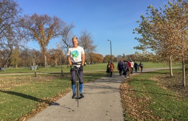 Man on a pogo stick in a park with a large group behind him