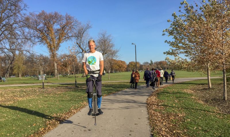 Man on a pogo stick in a park with a large group behind him