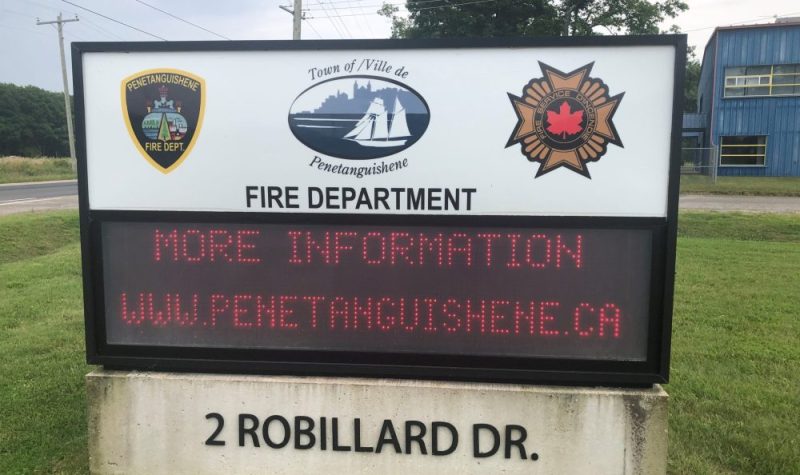 On peut voir le panneau numérique de la caserne de pompier de Penetanguishene. Les symboles de la ville et des pompiers y sont affichés et la section numérique affiche l'adresse du site web de la ville. À l'arrière on peut voir le gazon du terrain de la caserne.